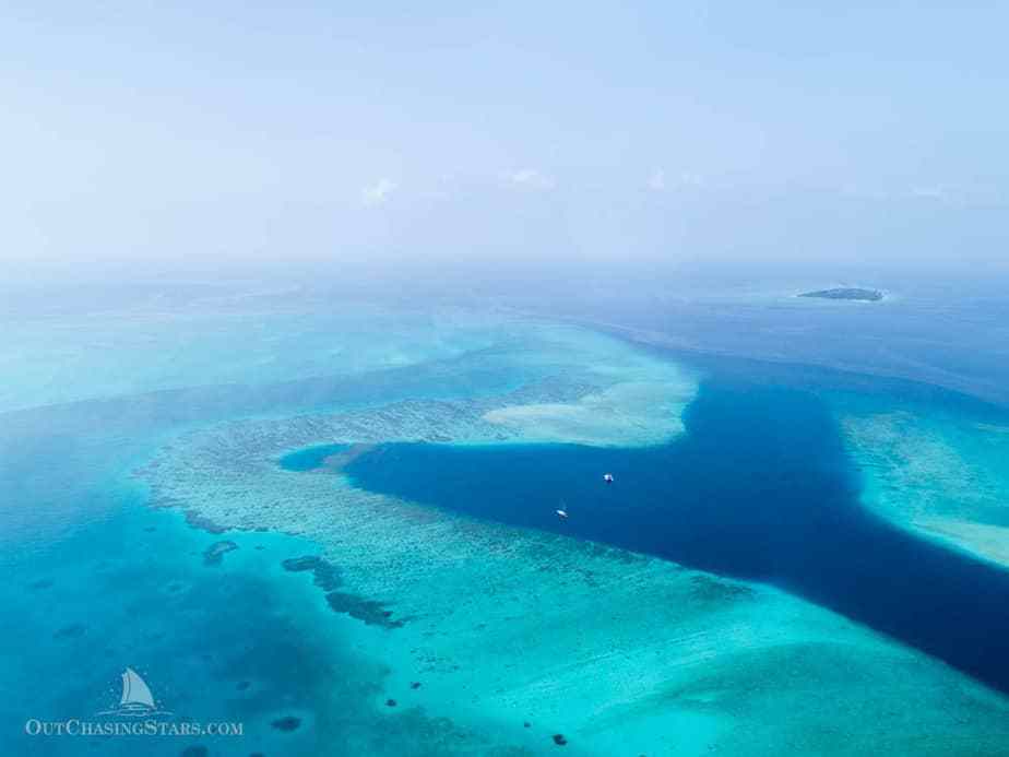 aerial view of a reef pass and protected anchorage with two yachts anchored in deep blue water surrounded by light turquoise water